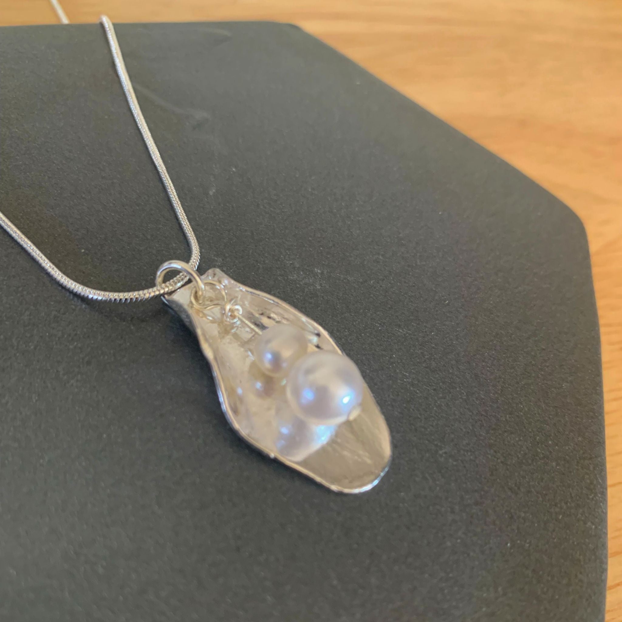 A completed fine silver pendant with a textured surface, displayed on a black stand, reflecting light from within its design.