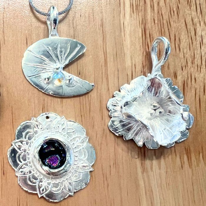 Three PMC silver pendants on a wooden surface from PMC Level 2 class