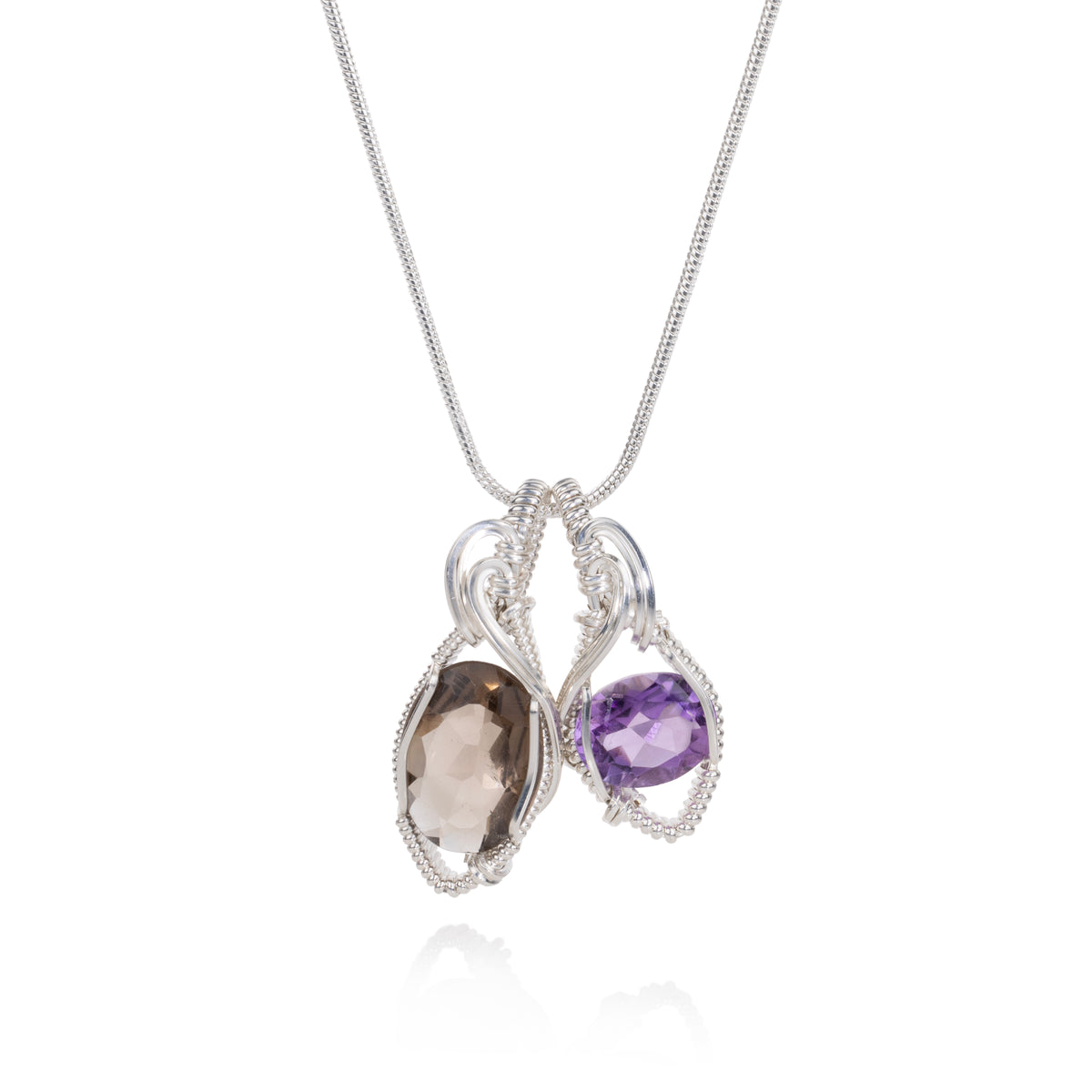 A silver pendant necklace featuring two teardrop-shaped gemstones, one smoky brown and one purple, set in a delicate wirework design on a white background.
