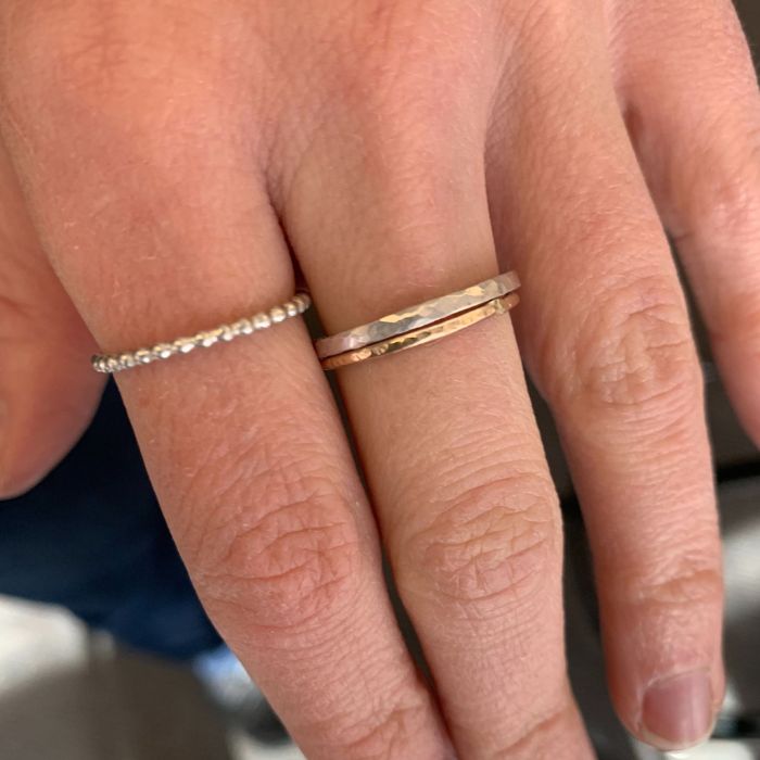 Close-up of a hand wearing two gold rings on a blurred background