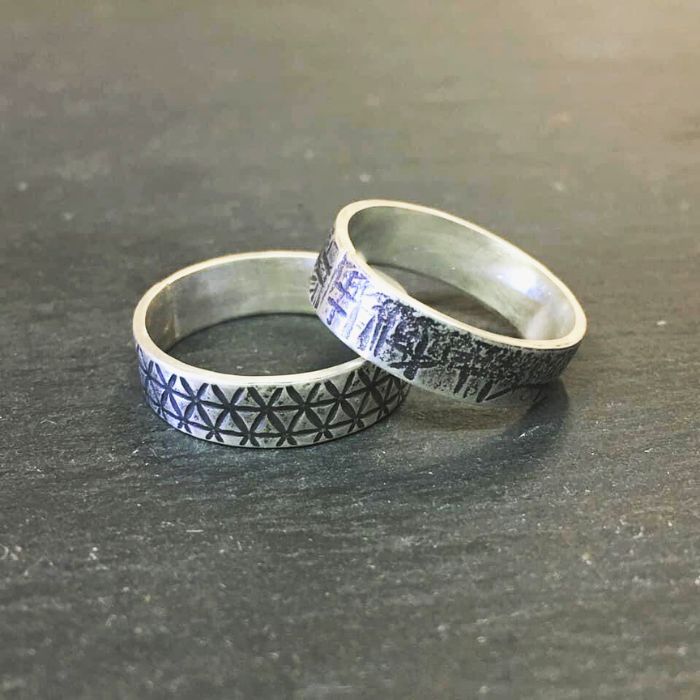 Two silver rings with geometric patterns on a dark surface