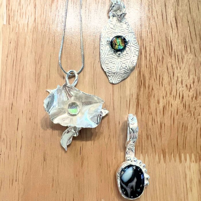 Three PMC silver pendants with gemstones on a wooden surface