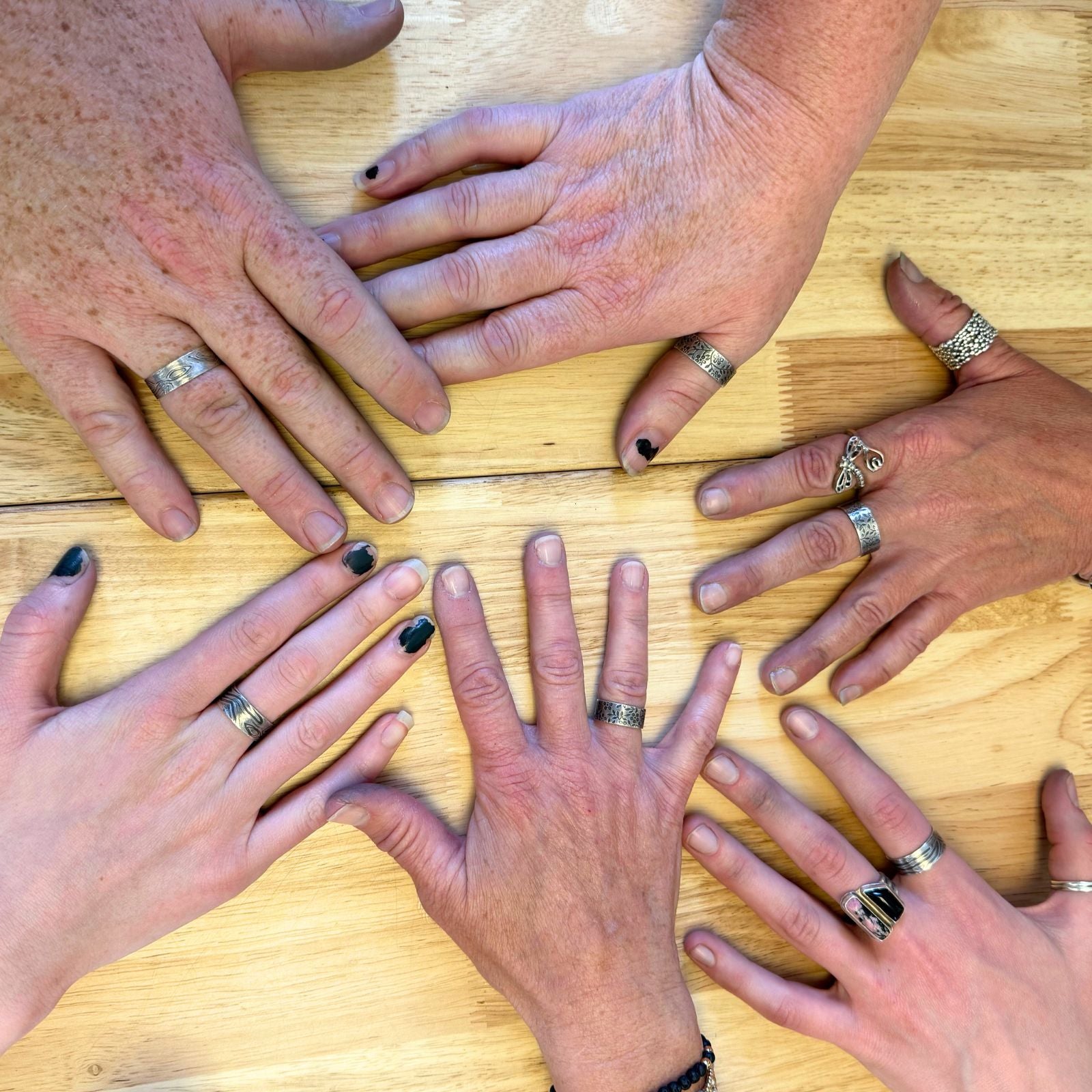 Hands with rings arranged in a circle on a wooden surface showing completed silver rings from Metals 1