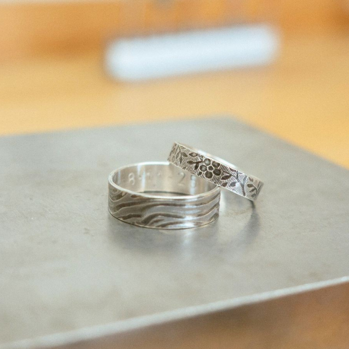 Two silver rings with intricate designs on a metallic surface.