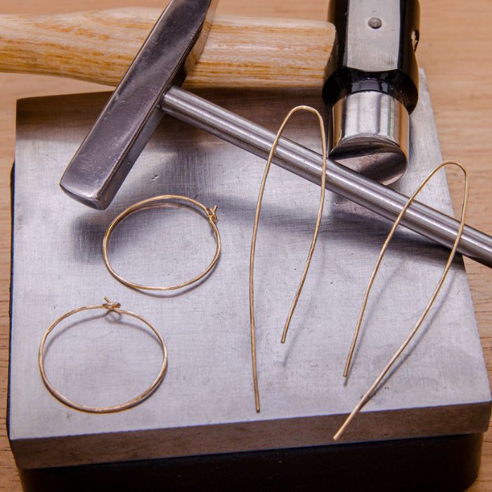 Gold hoop earrings and wire on a metal surface with pliers