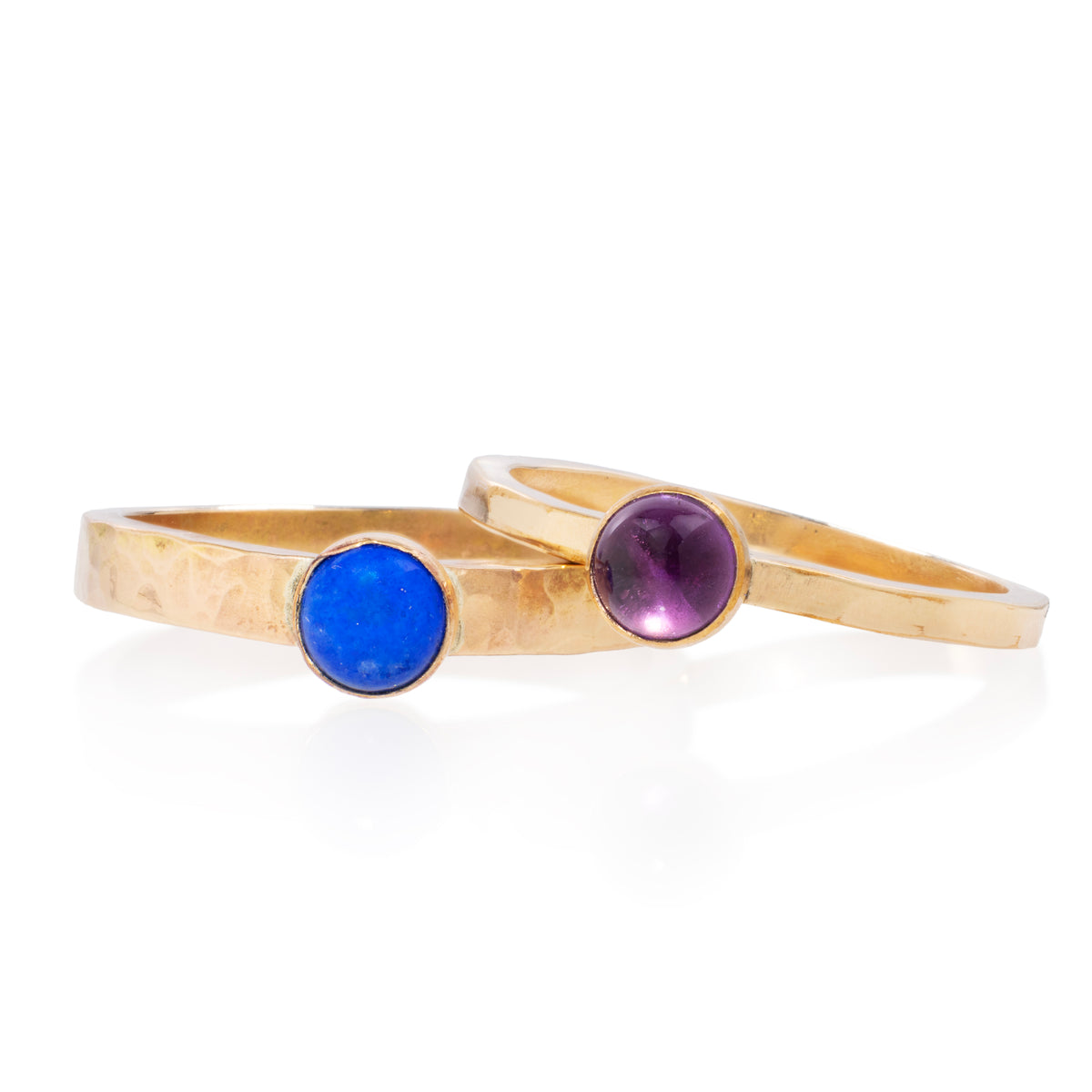 Two hammered gold bands with round bezel-set gemstones, one blue and one purple, displayed on a clean white background.